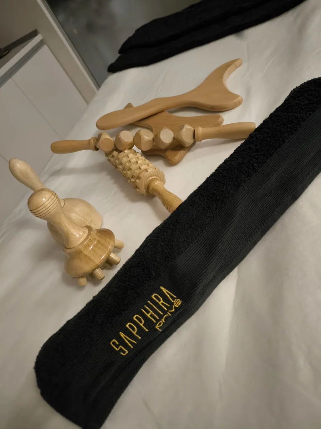 Utensilios de maderoterapia sobre una camilla con una toalla negra bordada con el logotipo de Sapphira Privé